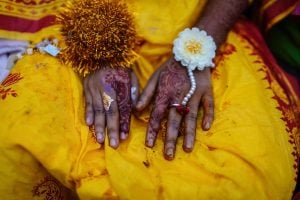 A view of a girl's lap, dressed in bright yellow with hands decorated for a traditional Bangladeshi wedding