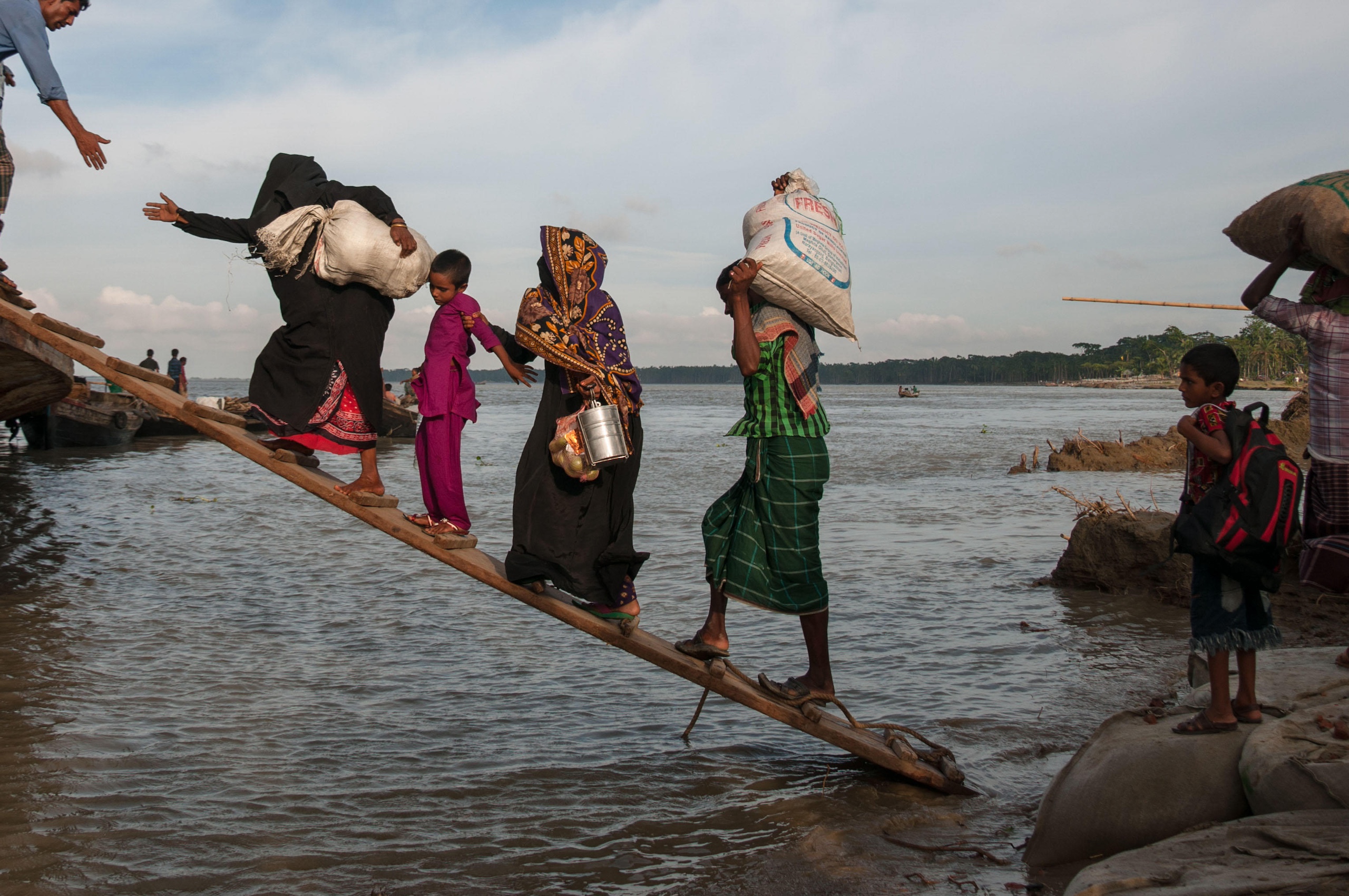 People walk up a gang plank over flood waters, carrying their belongings