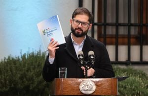 President Gabriel Boric holding up book behing lectern