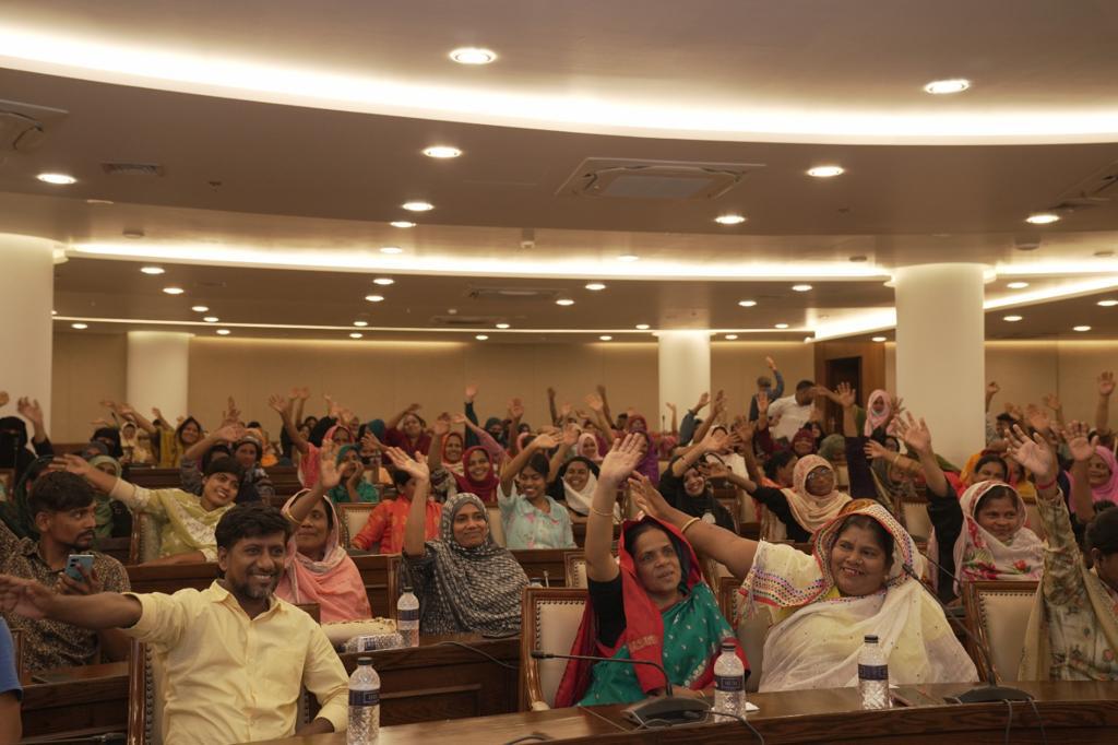 People sat in an auditorium raise their hands and smile