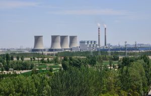 A power plant with towering chimneys amidst a backdrop of lush green trees