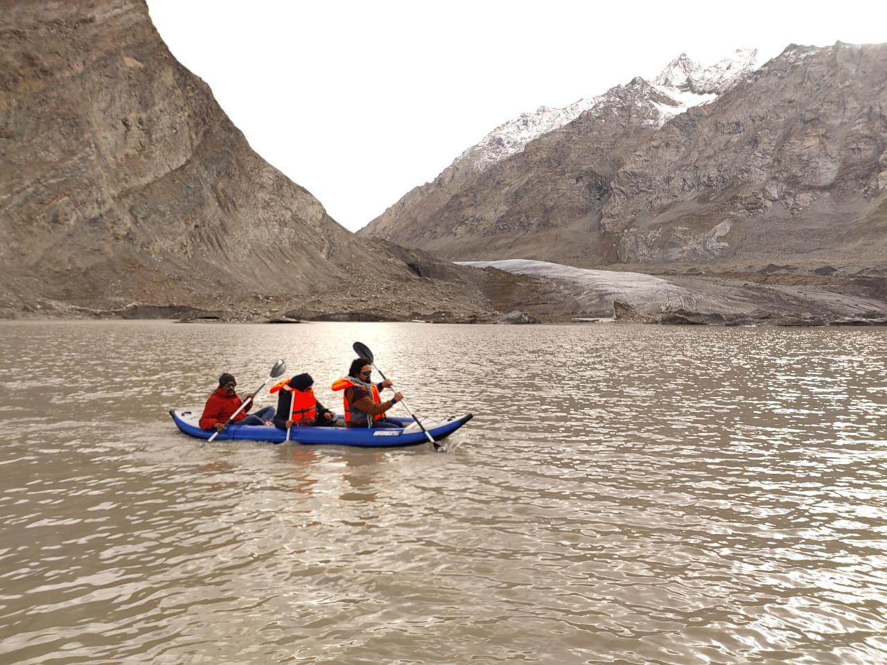 Three people in a canoe paddling on a lake in a mountainous area