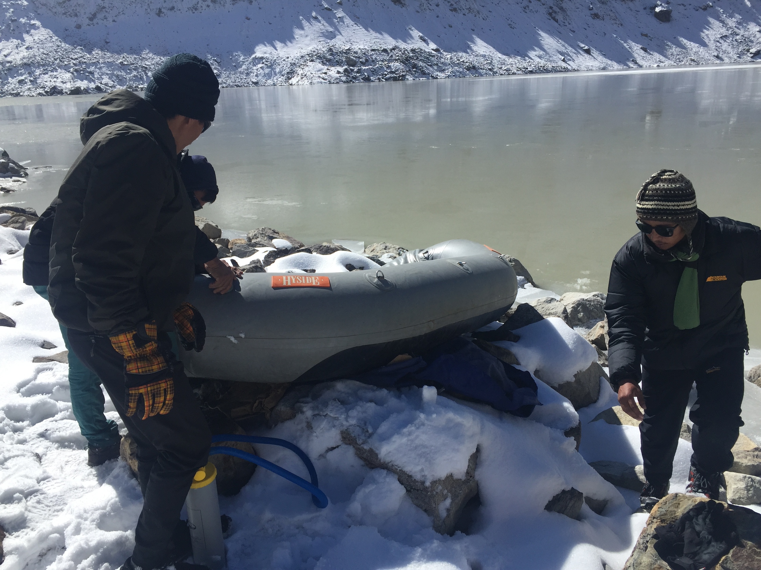 Two people inspect a dinghy next to a lake in a snowy mountainous area