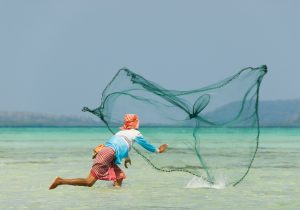 Person throwing a fishing net into turquoise sea