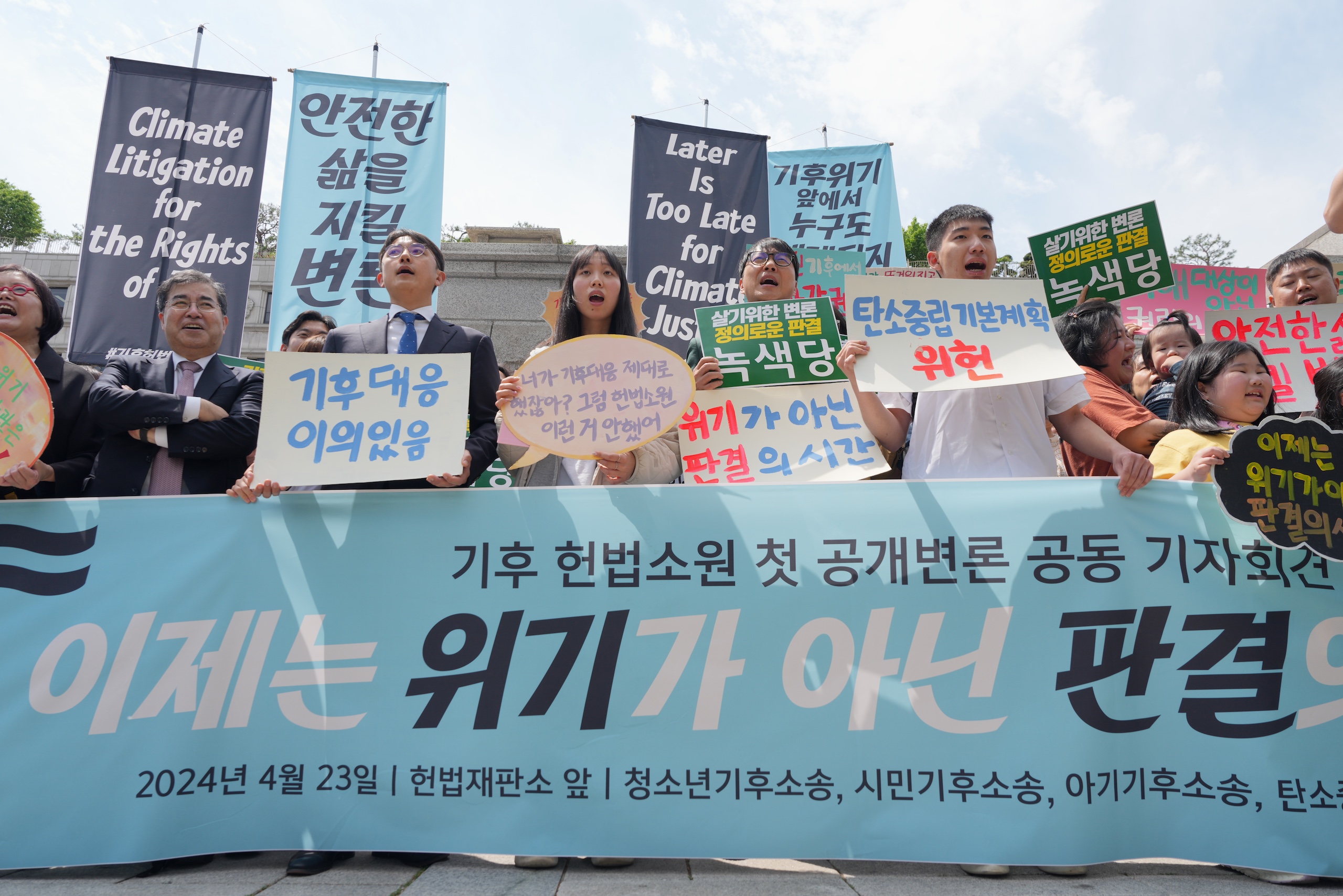 A group of people behind a banner holding placards and signs and chanting