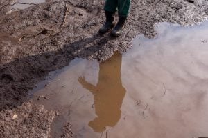 Reflection of man on surface of mud puddle