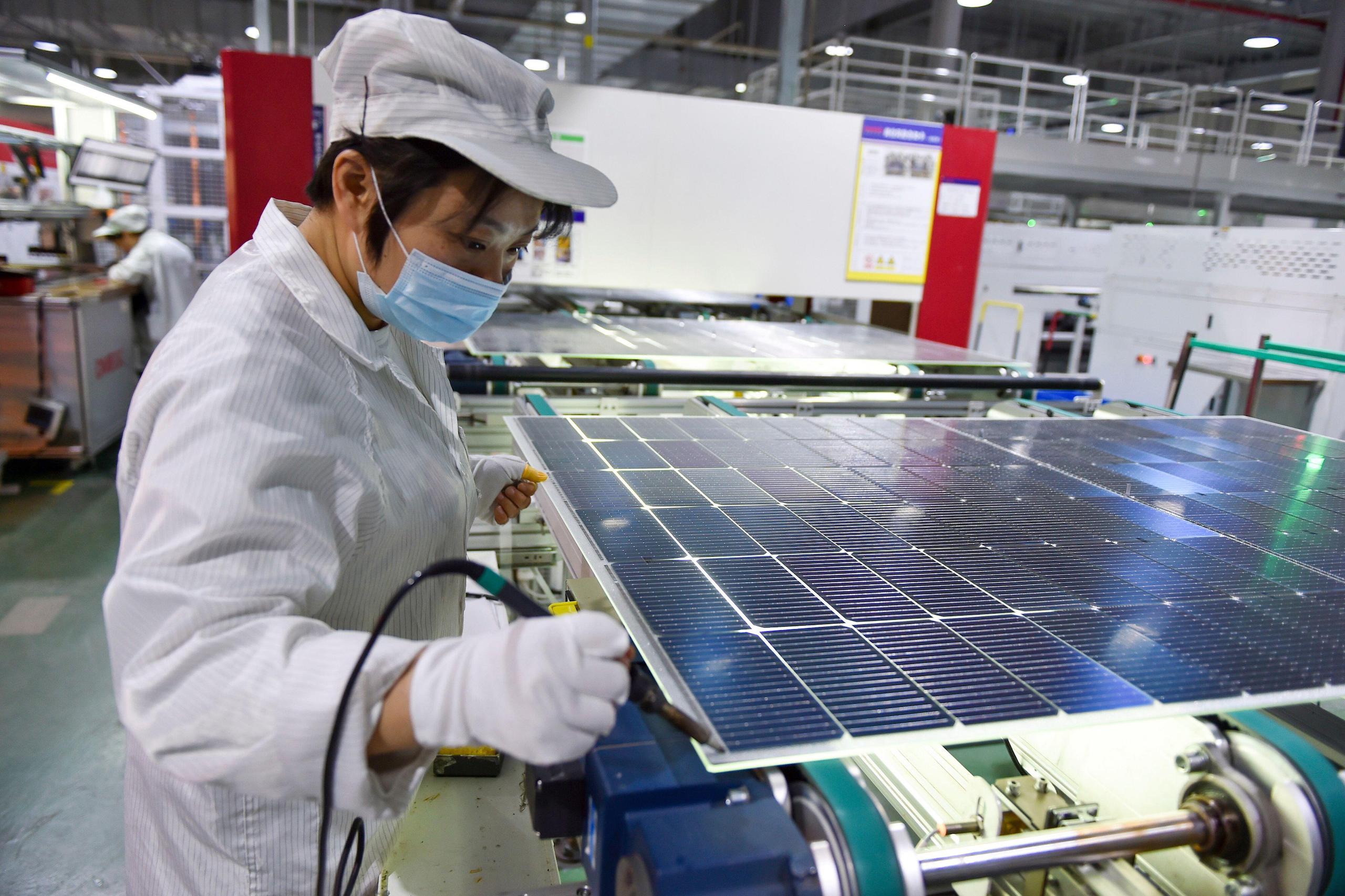 A worker in a white coat working on a solar panel