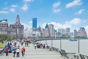 People walking along the river side under a blue sky dotted with white clouds