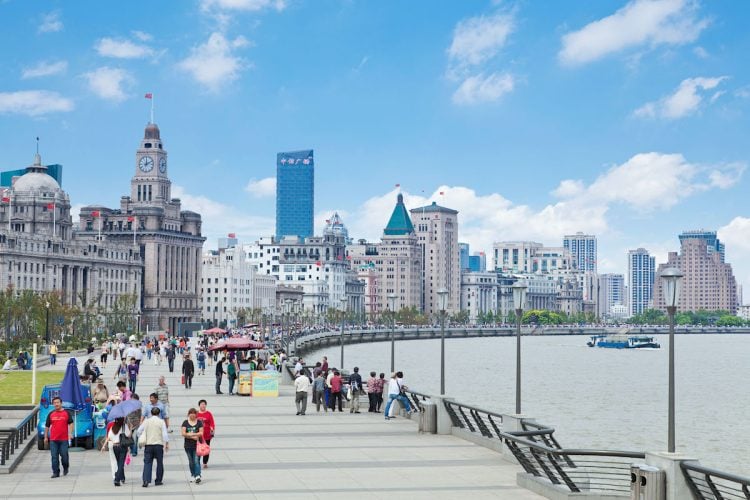 People walking along the river side under a blue sky dotted with white clouds