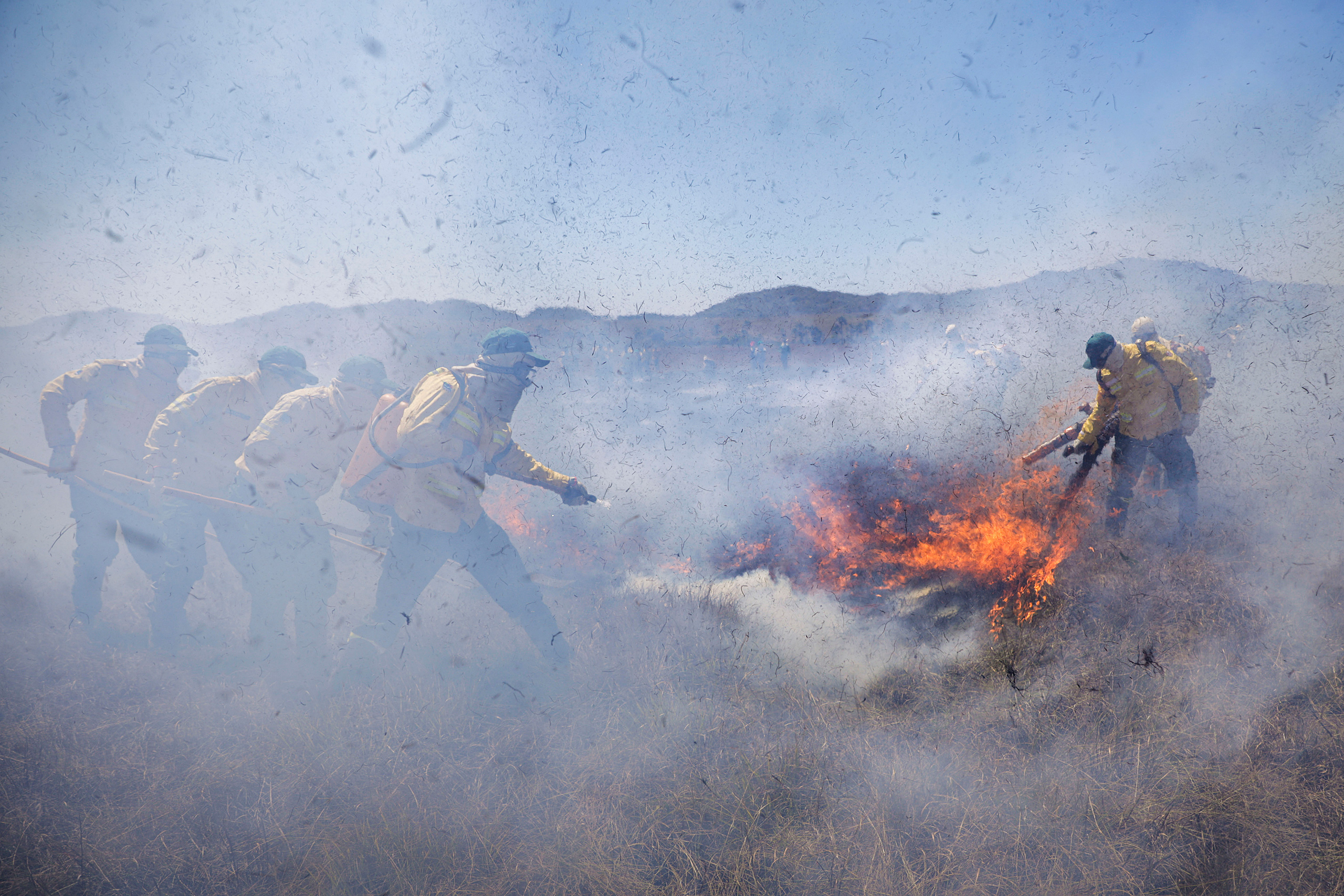 Bomberos con trajes amarillos apagando un incendio en una zona montañosa