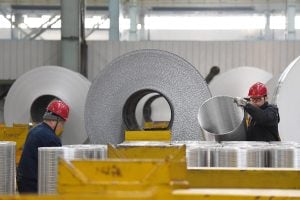 Factory workers handling aluminum rolls in manufacturing plant