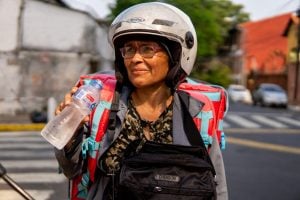 Una mujer en una moto y con un casco toma agua