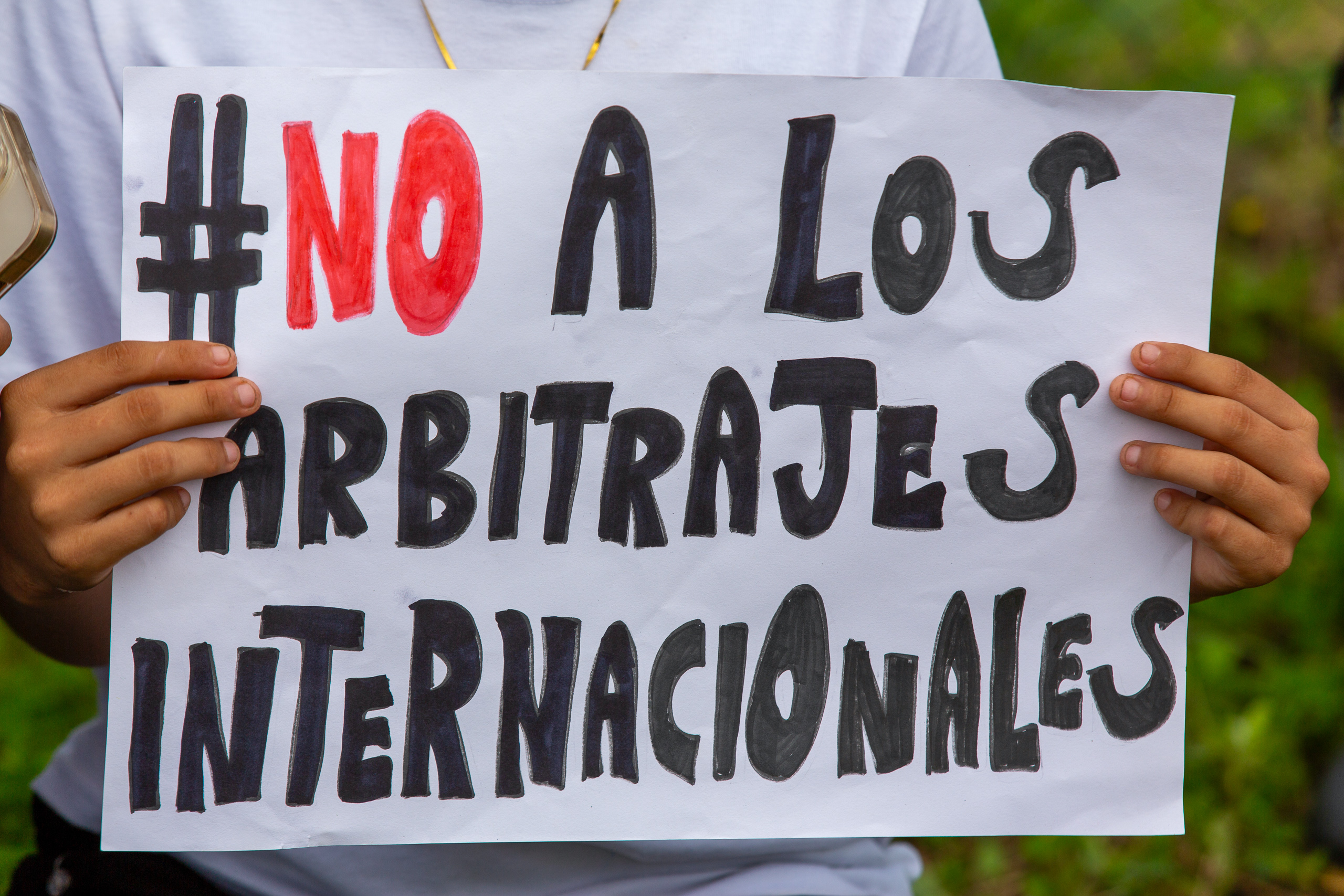 Una persona sosteniendo un cartel que dice "no a los arbitrajes internacionales"