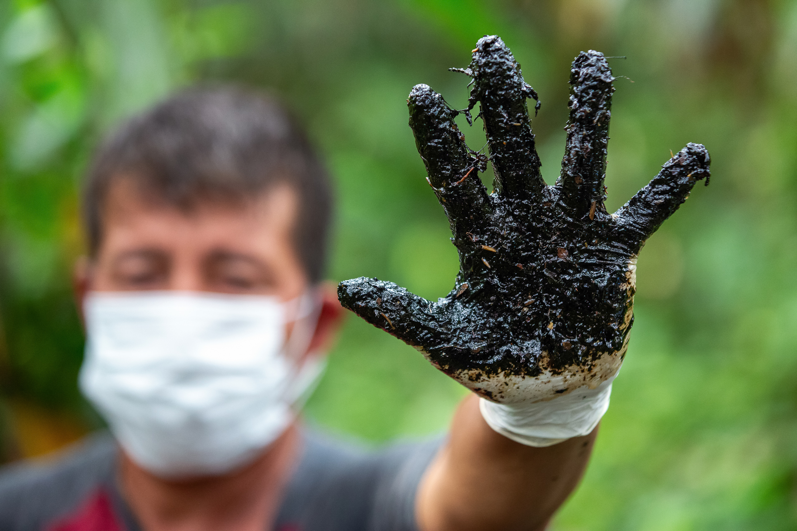 Un hombre con máscara y guantes levanta una mano cubierta de petróleo