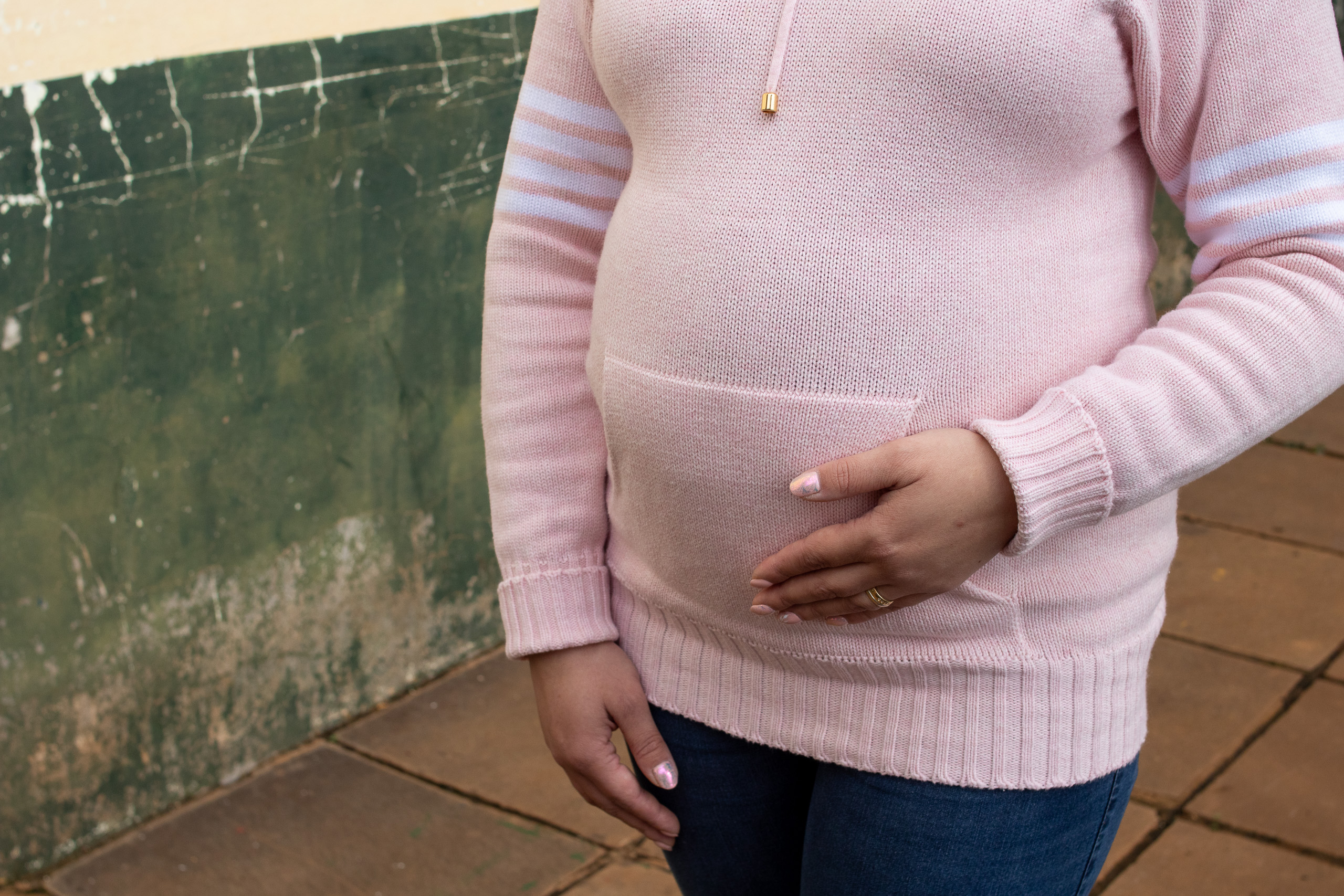 mujer embarazada con una camiseta de punto rosa y su mano en el vientre