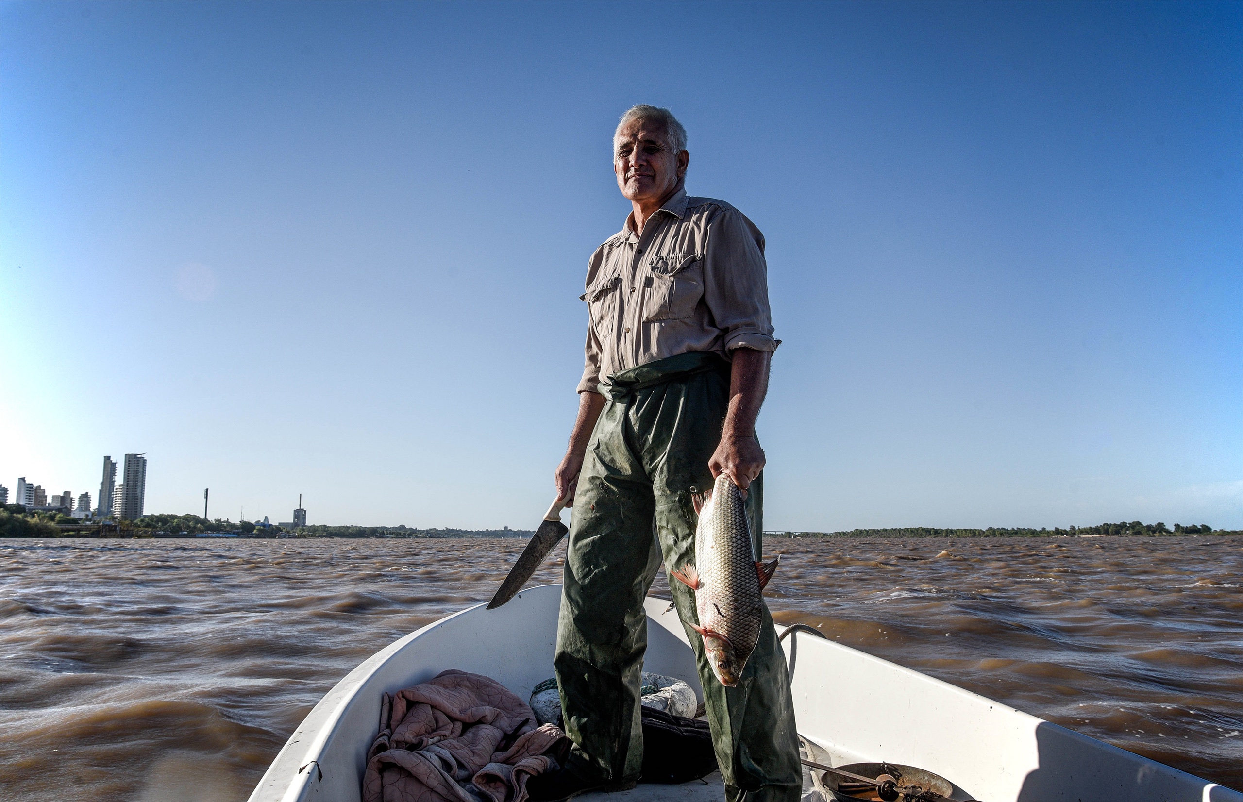 a man in a small boat holds up a fish he has just caught