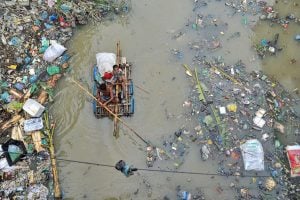 A man and a child navigate a boat through a river cluttered with debris and garbage