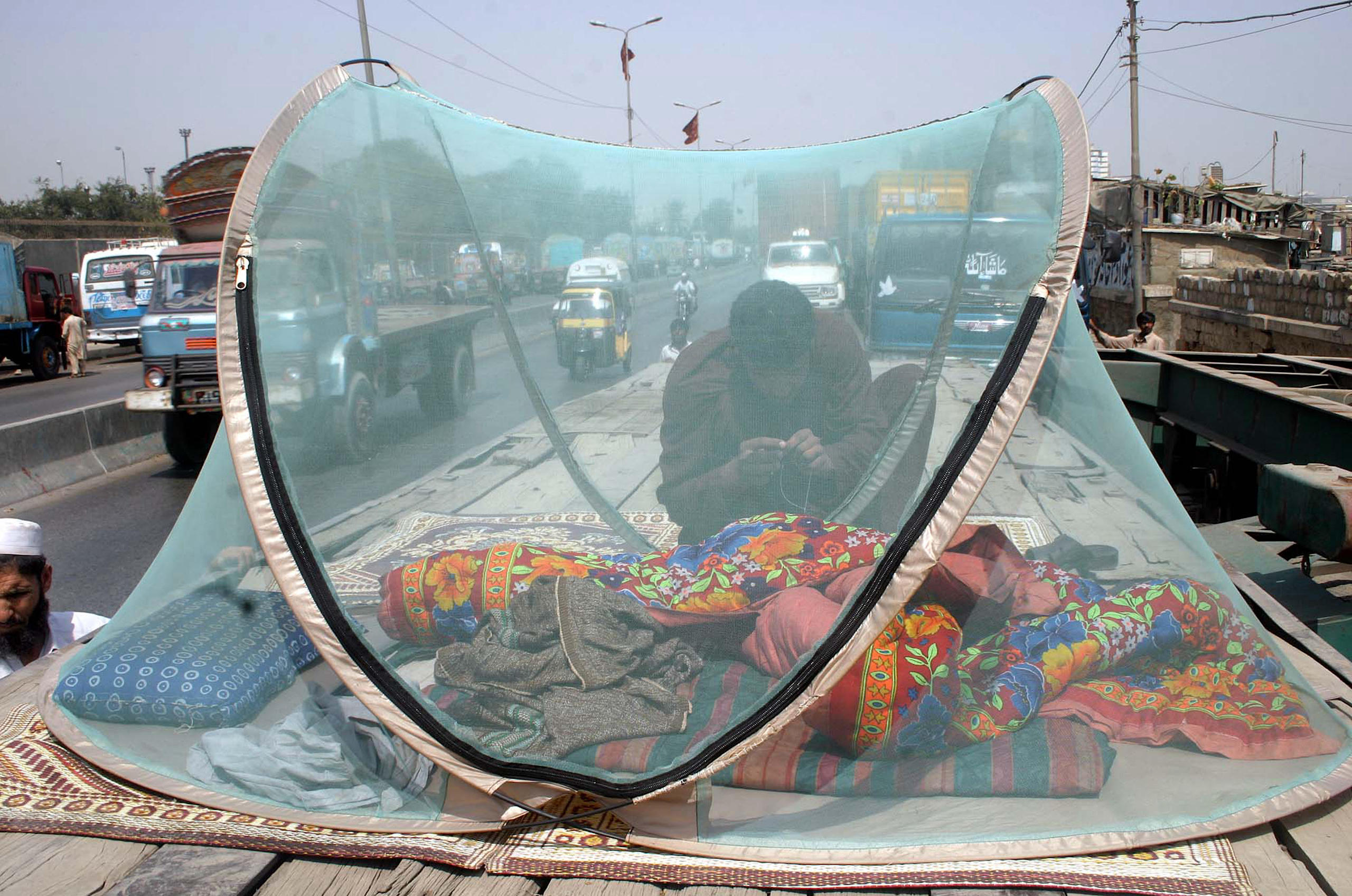 <p>A homeless labourer arranges a mosquito net over his temporary bed on a truck at a roadside in Karachi, Pakistan (Image: Owais Aslam Ali / PPI / Alamy)</p>