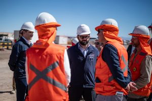 A group of men wearing hard hats and vests engaged in conversation at a construction site