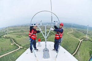 Two men standing atop a wind turbine, working on repairs