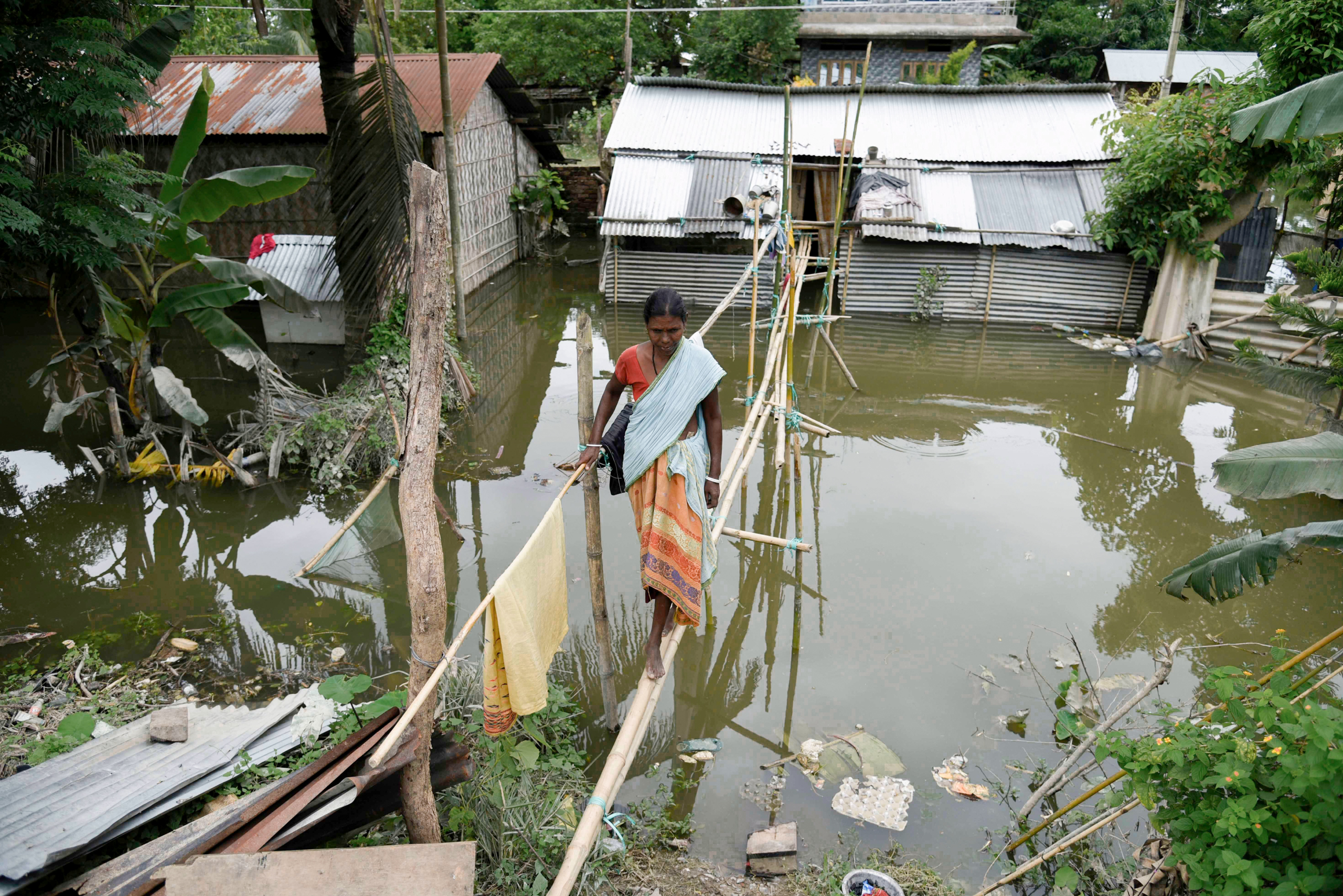 <p>A woman crosses a temporary bridge in a flood-affected village in Assam, north-east India, in July 2020. Four years on, another monsoon flood had killed a reported 117 people in Assam by 25 July, yet India has barely begun legislating against building in flood-risk zones. (Image: David Talukdar / ZUMA Wire / Alamy Live News)</p>