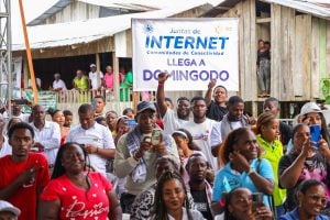 Grupo de personas sonriendo, con un cartel detrás que dice "Juntas de Internet, Comunidades de Conectividad llega a Domingodo"