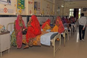 line of single beds in hospital, each occupied by multiple people