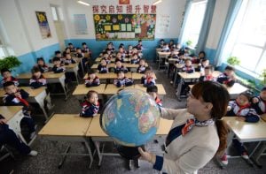 woman holding globe in front of classroom of children