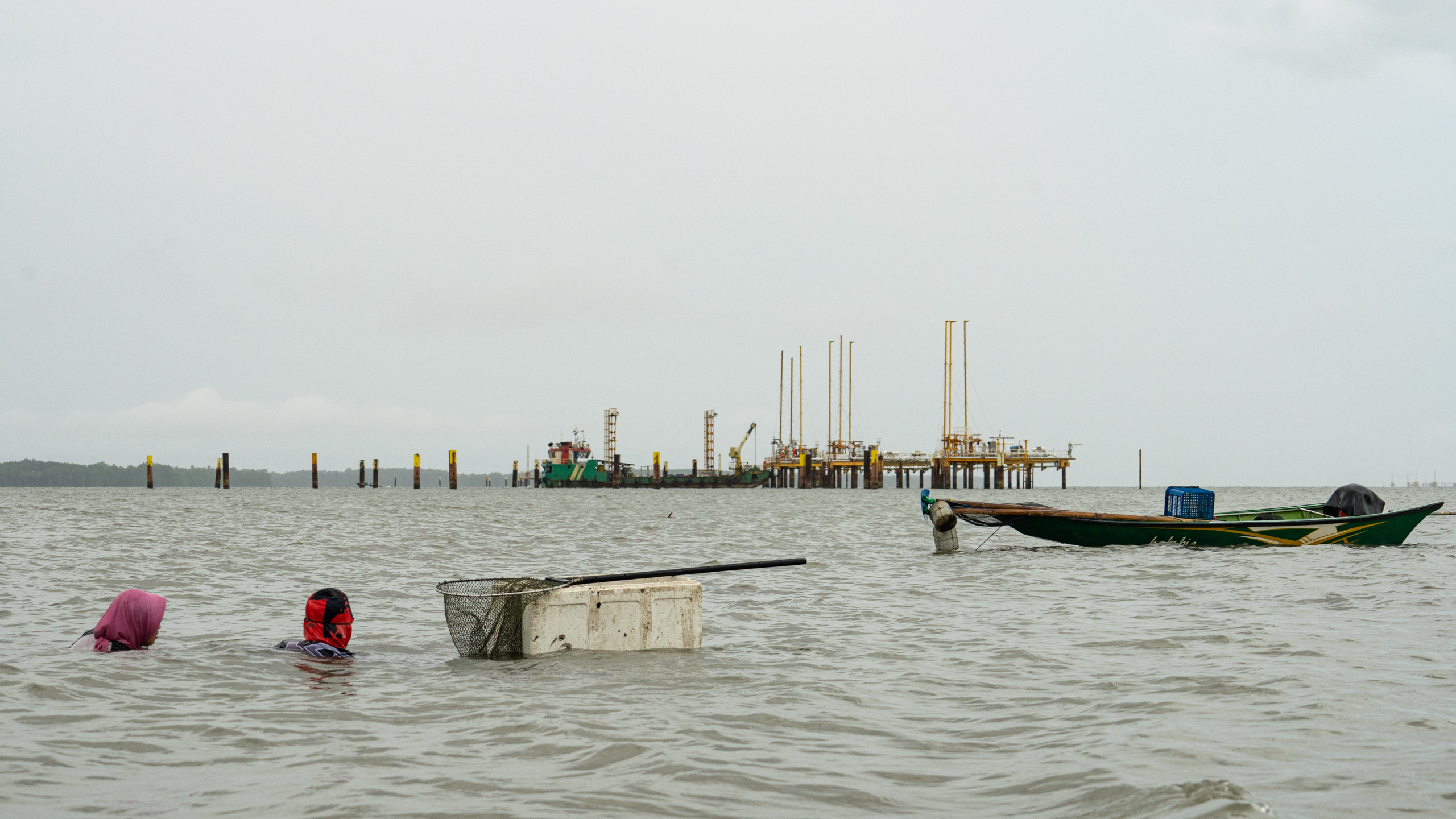 a fishing boat in the river with a gas well in the background