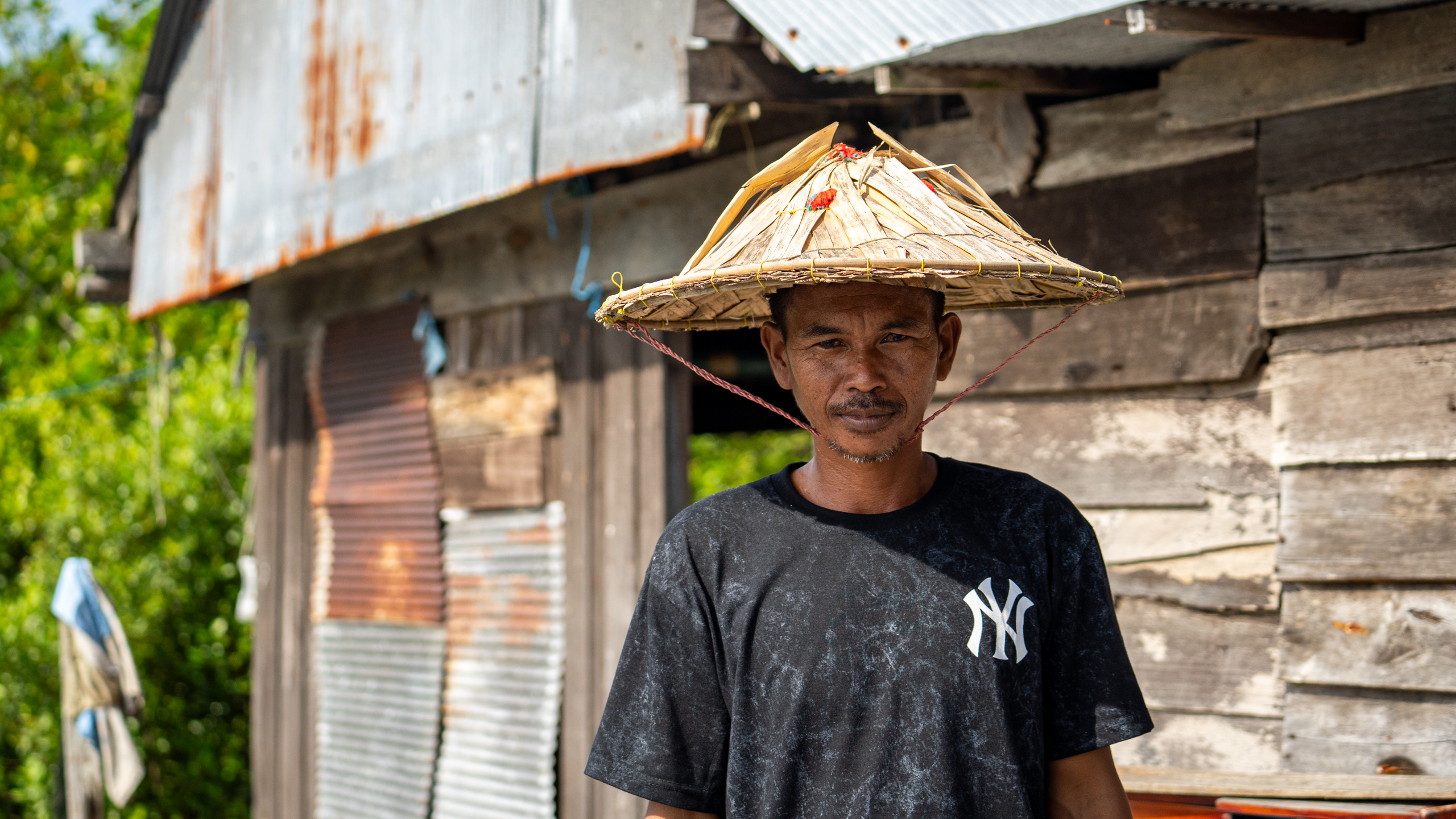 A man wearing a hat, standing in front of a house