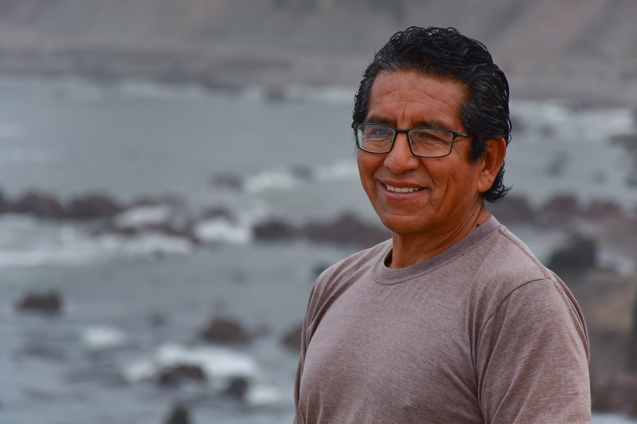 Un hombre con una remera gris y anteojos frente al mar