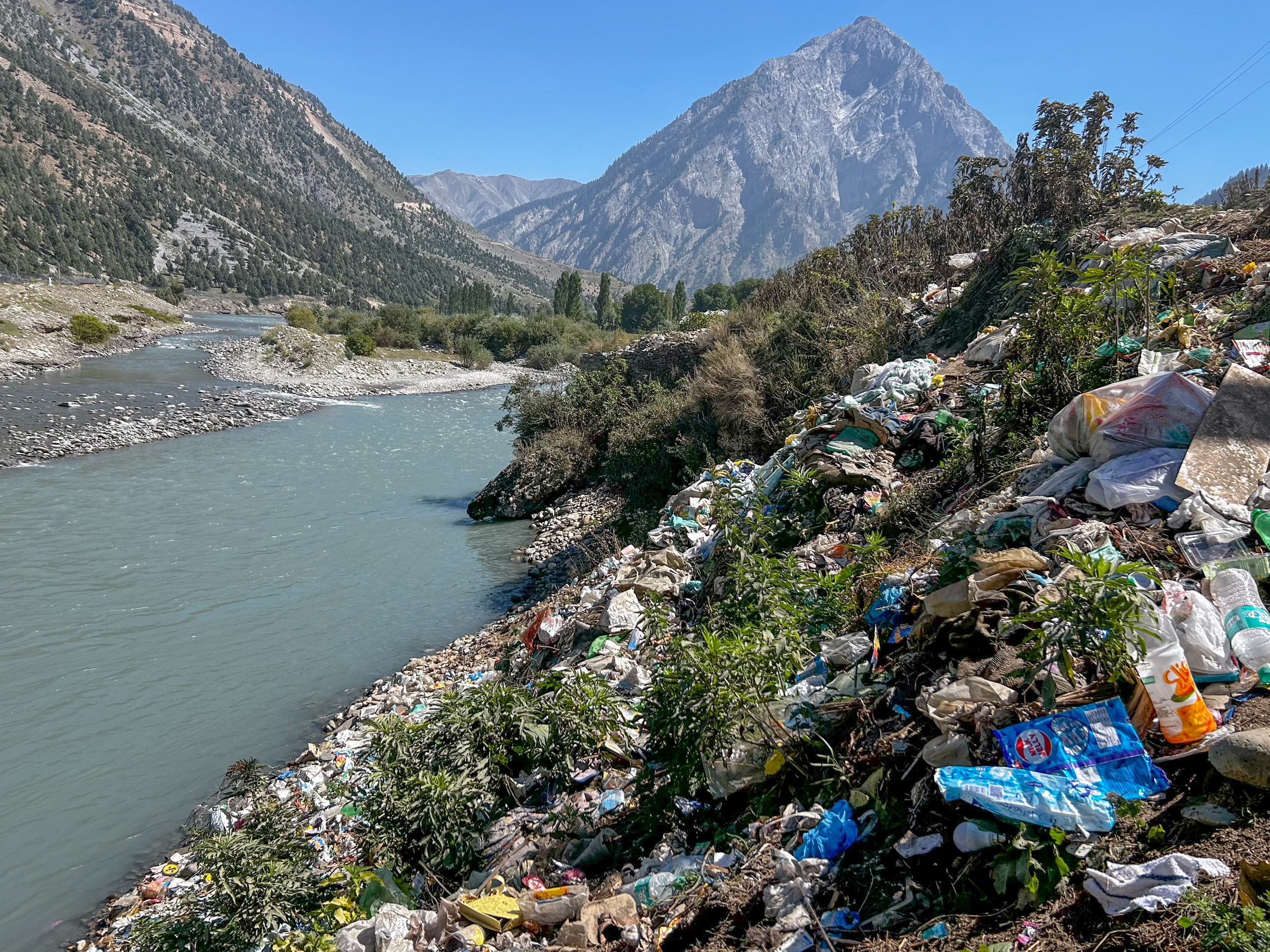 plastic waste near stream with mountain in background