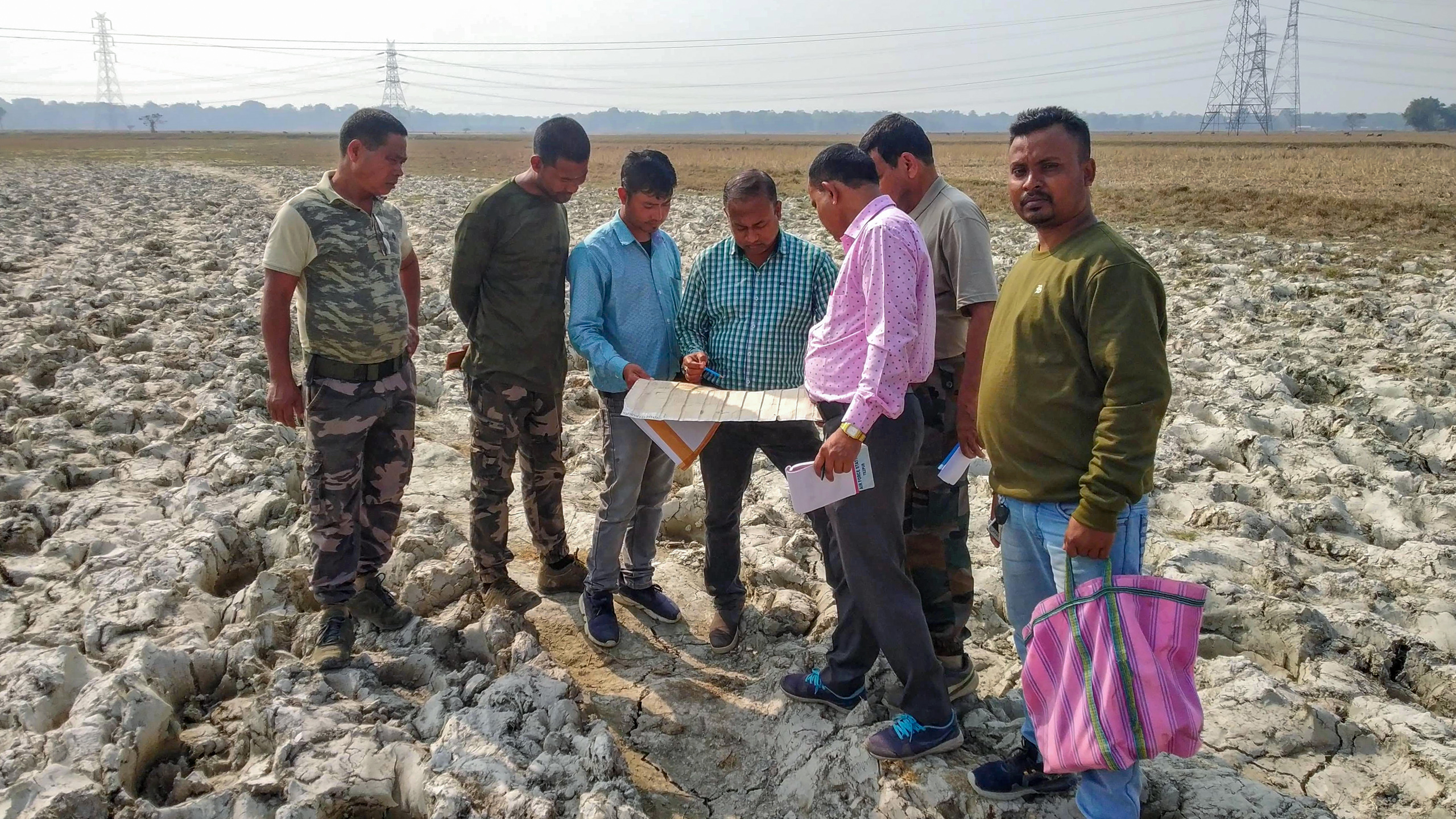 A group of men stands in a field, examining a map