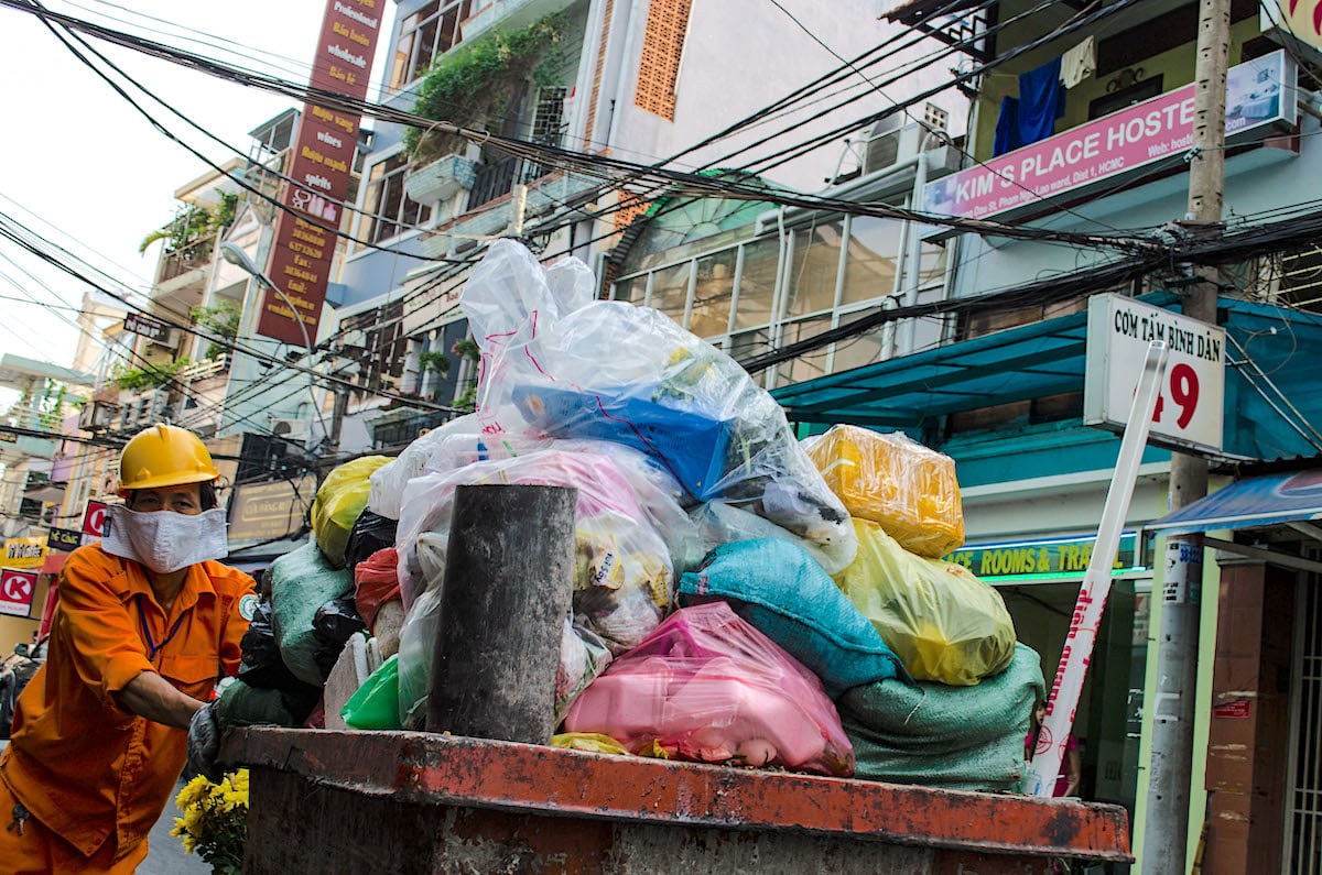 A man in an orange jumpsuit pushing a garbage collecting cart