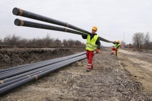 two men carry long electrical conduits on shoulders