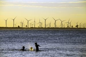 Niños jugando en el mar, frente a un parque eólico