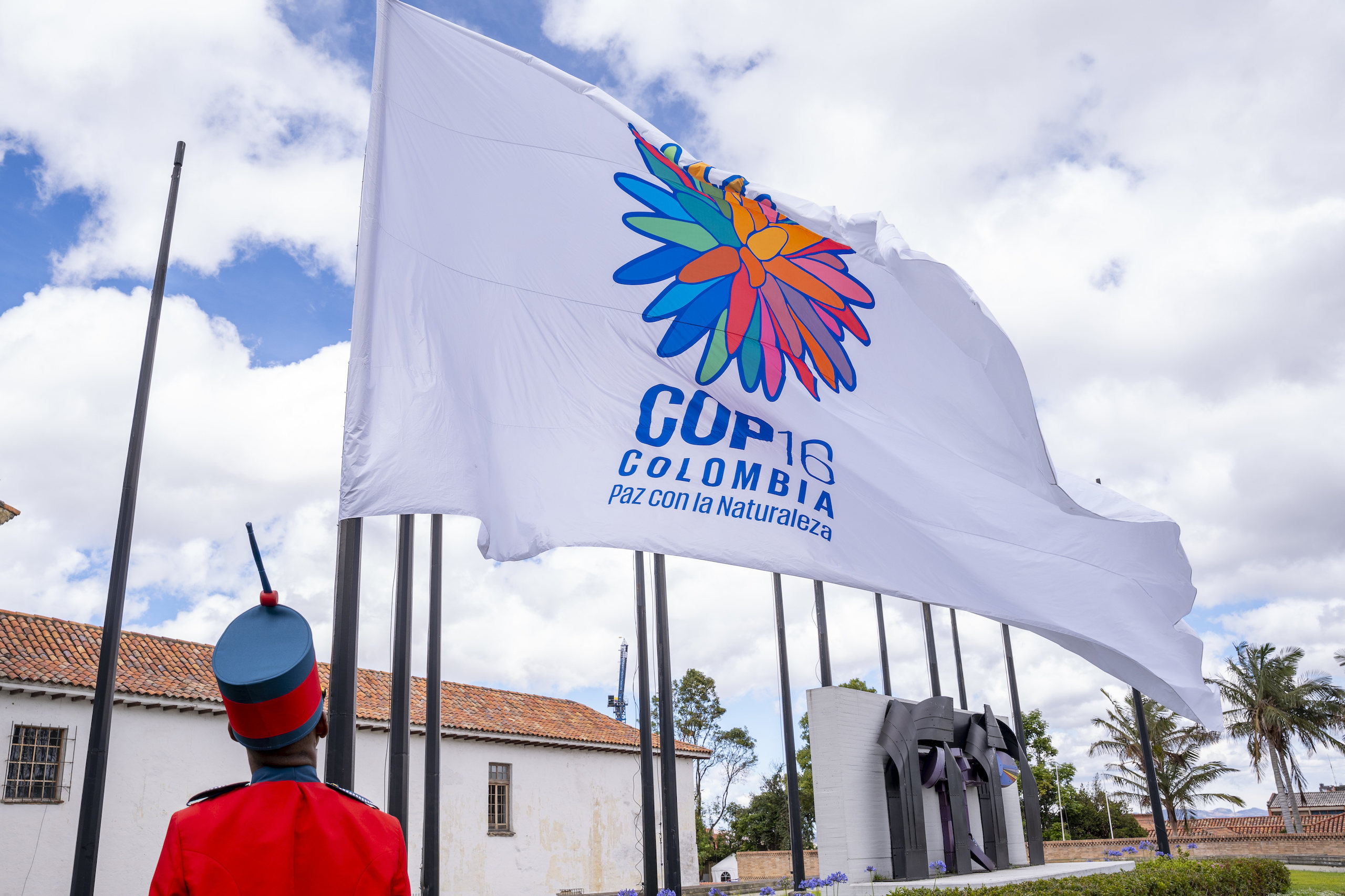Soldado com roupa vermelha e chapéu hasteia bandeira da COP16 em Bogotá