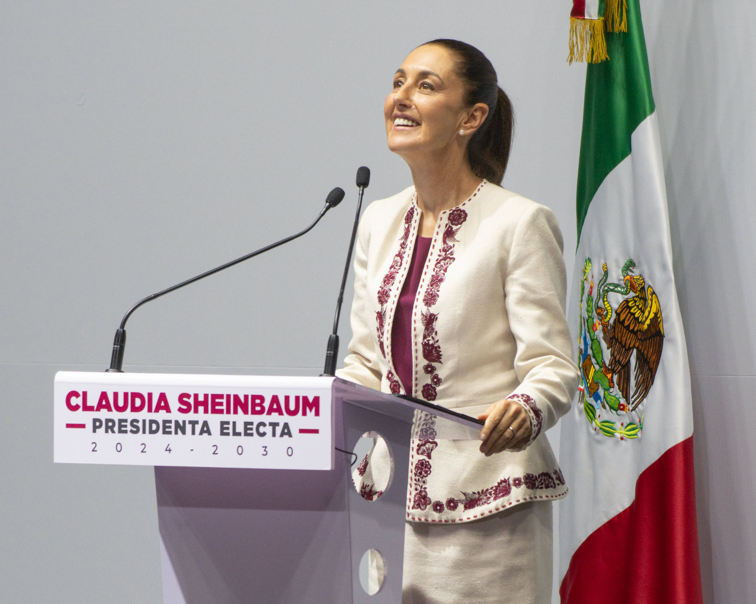 Nova presidente do México, Claudia Sheinbaum, sorri em palanque de vestido bege com detalhes roxos