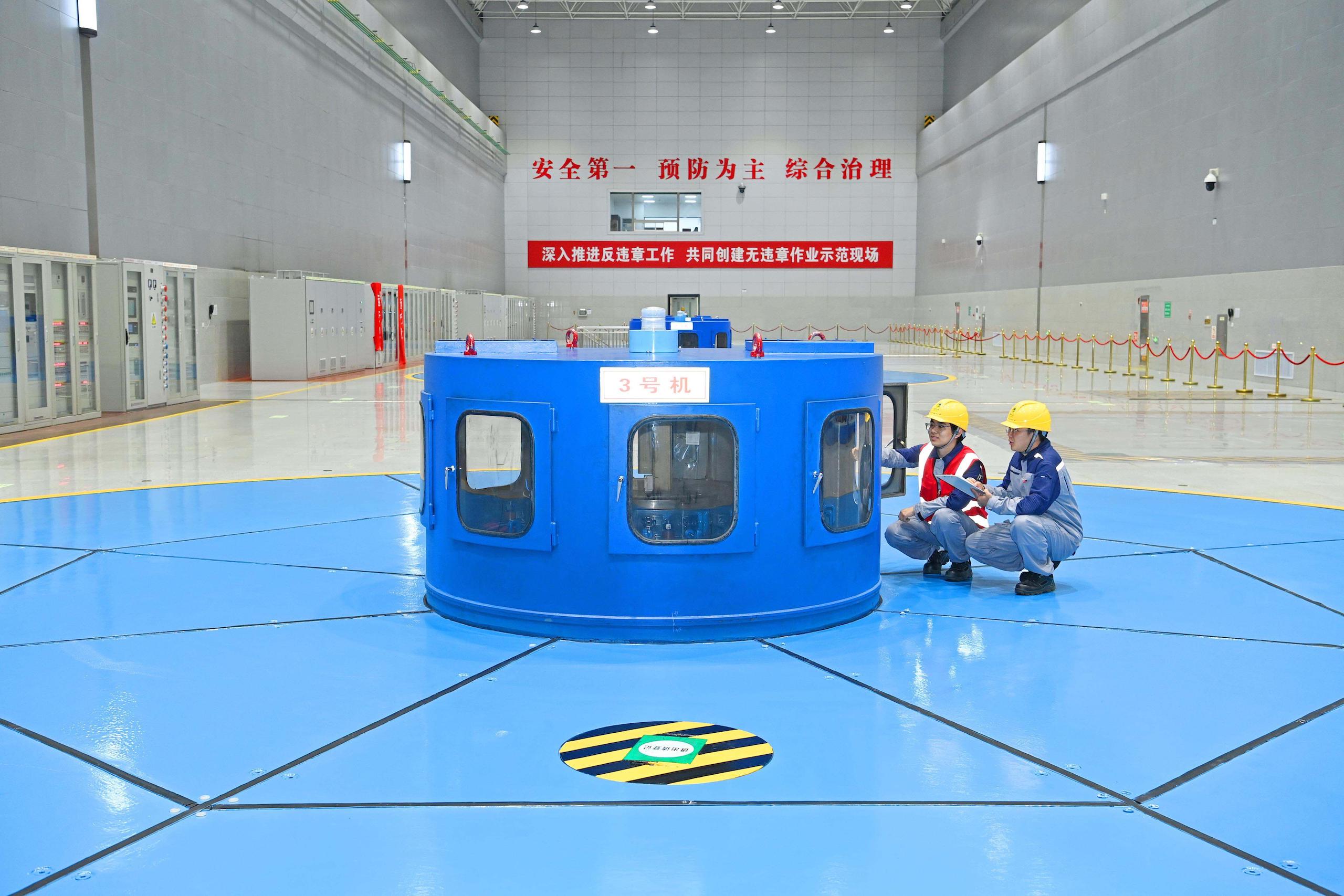 Two workers wearing hard hats are checking on a blue and white machine