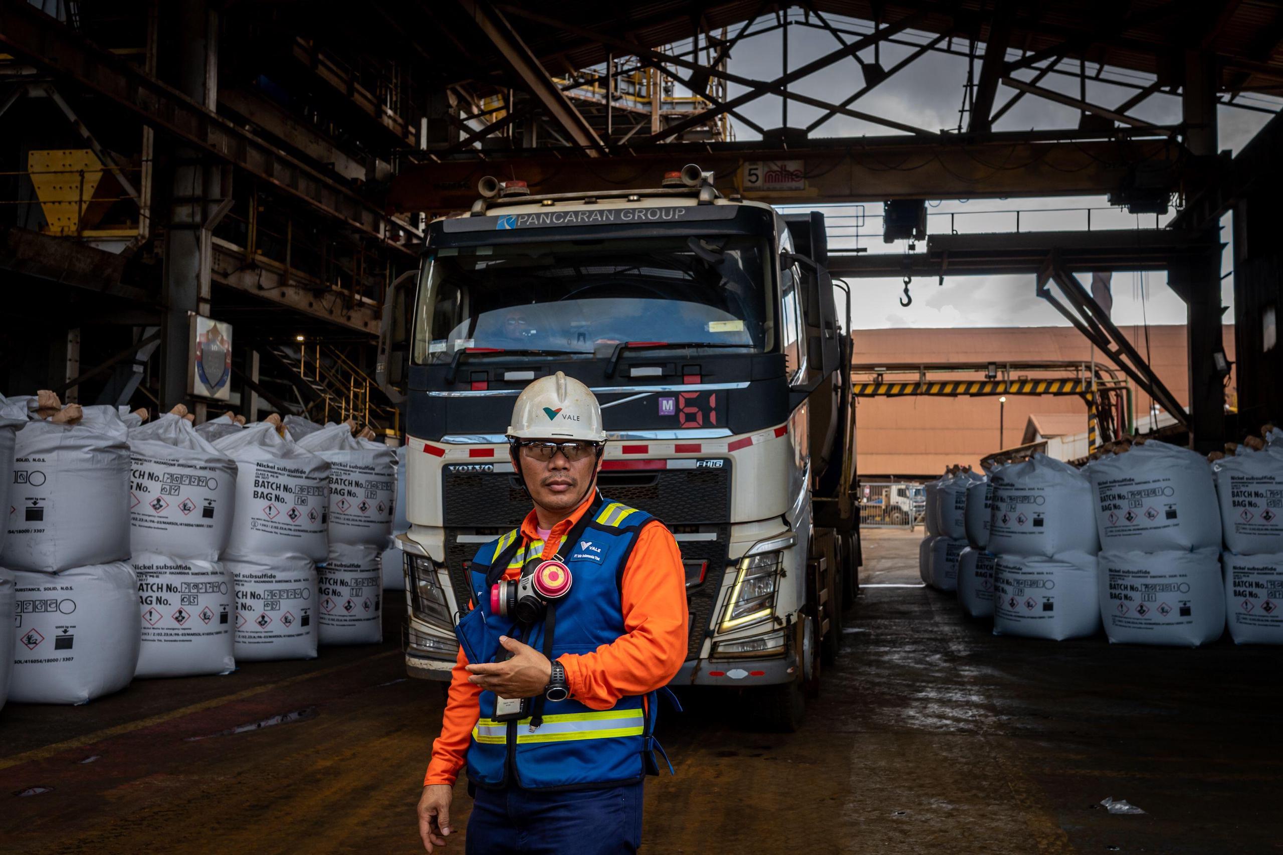 A worker stands in front of a large truck and nickel bags at a plant