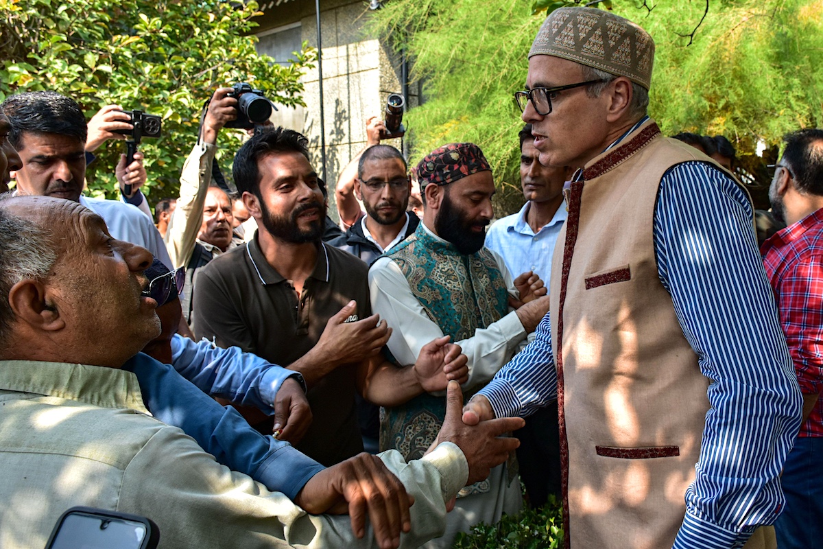 A man in traditional Kashmiri clothes shakes hands with a crowd of supporters, some of whom have cameras