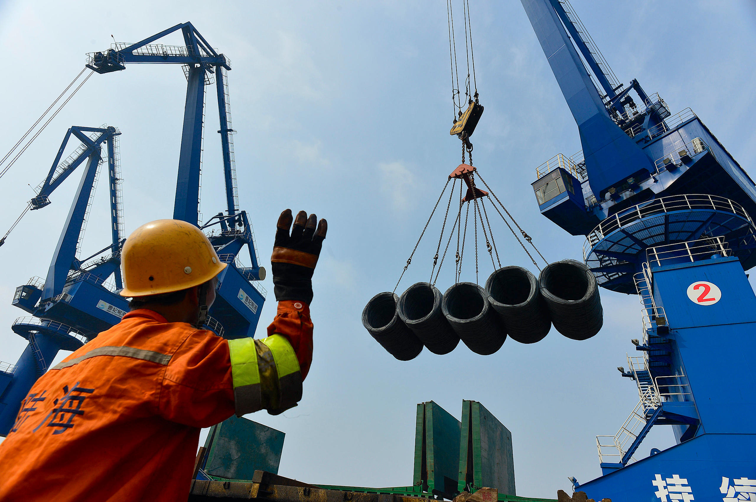 A worker giving instruction on transferring steel products by a crane