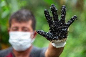 homen com máscara mostra mão suja de óleo