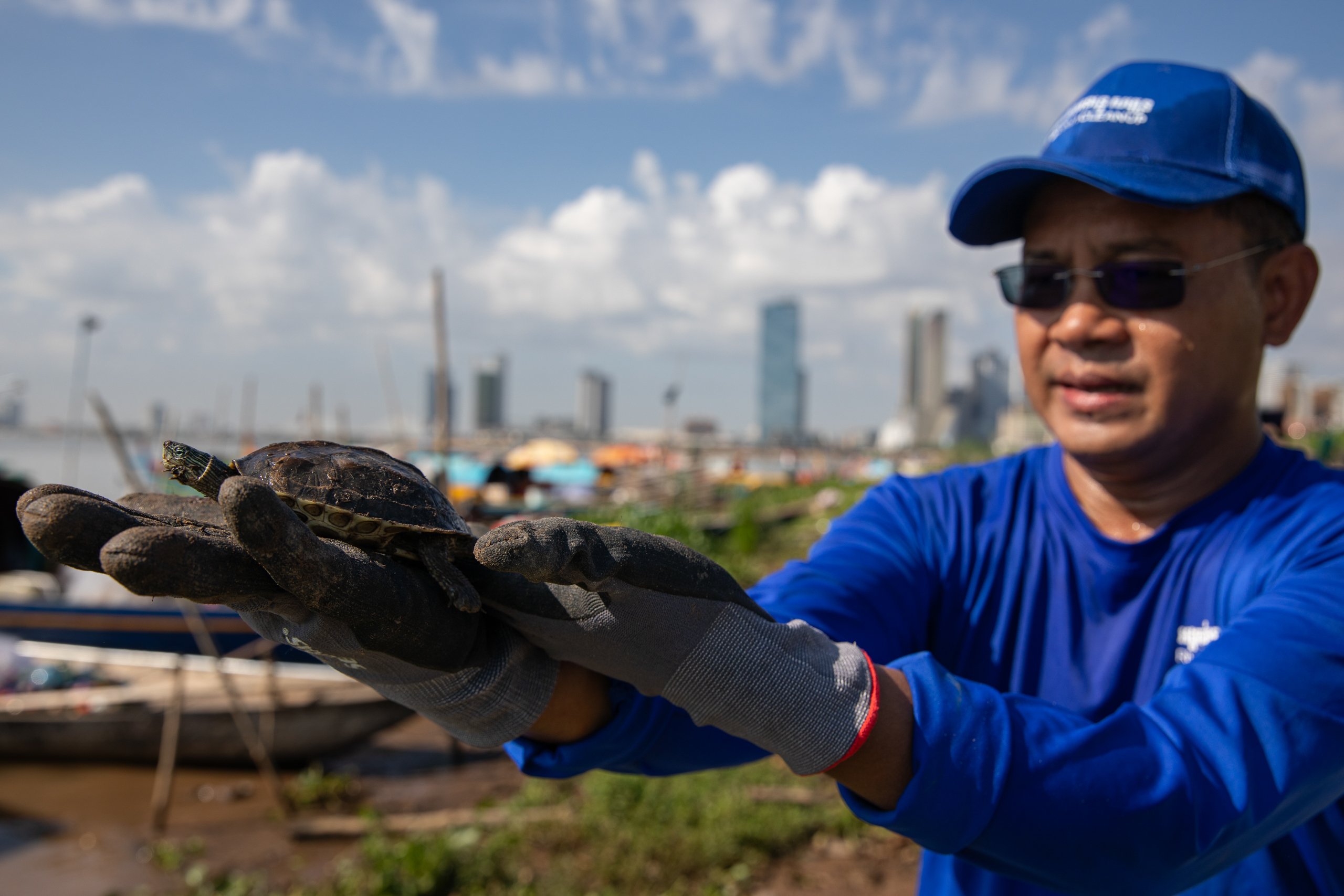 A man holds a turtle while standing next to water