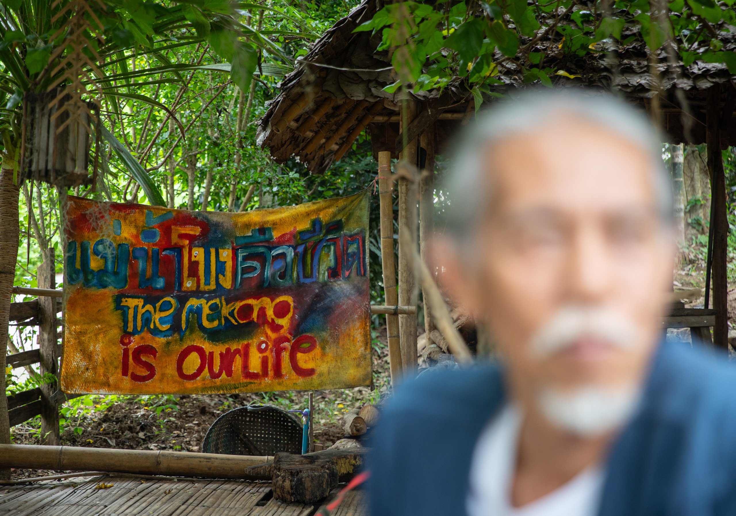 a man sits in front of a banner reads: “The Mekong is our life” 