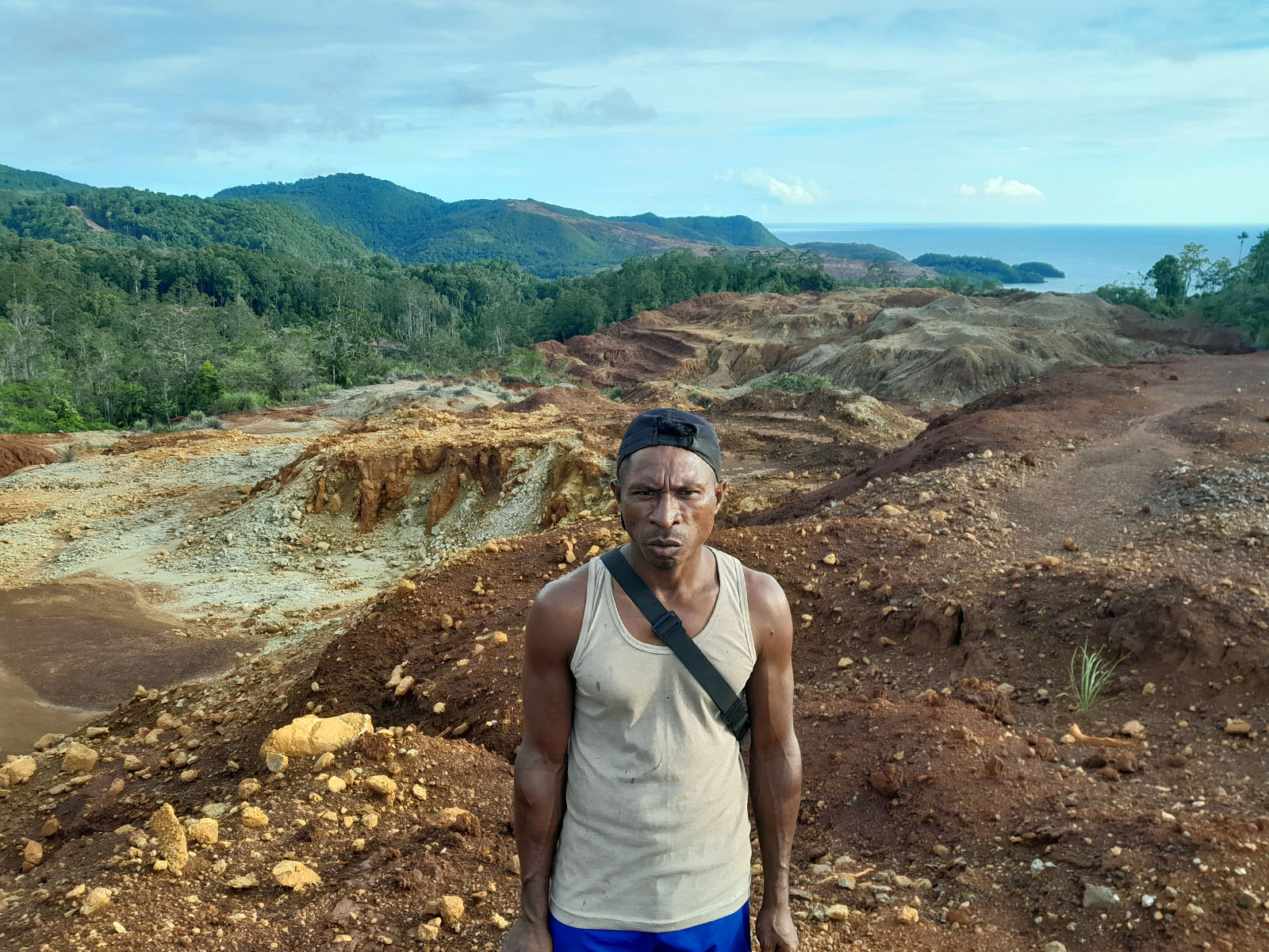 A man stands on a dirt road, surrounded by mountains