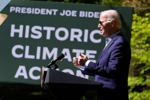 Joe Biden in suit speaking at podium with sign reading "HISTORIC CLIMATE ACTION"