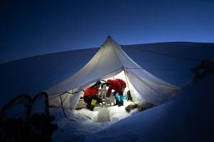 Two people are inside a tent doing research in a snowy mountain