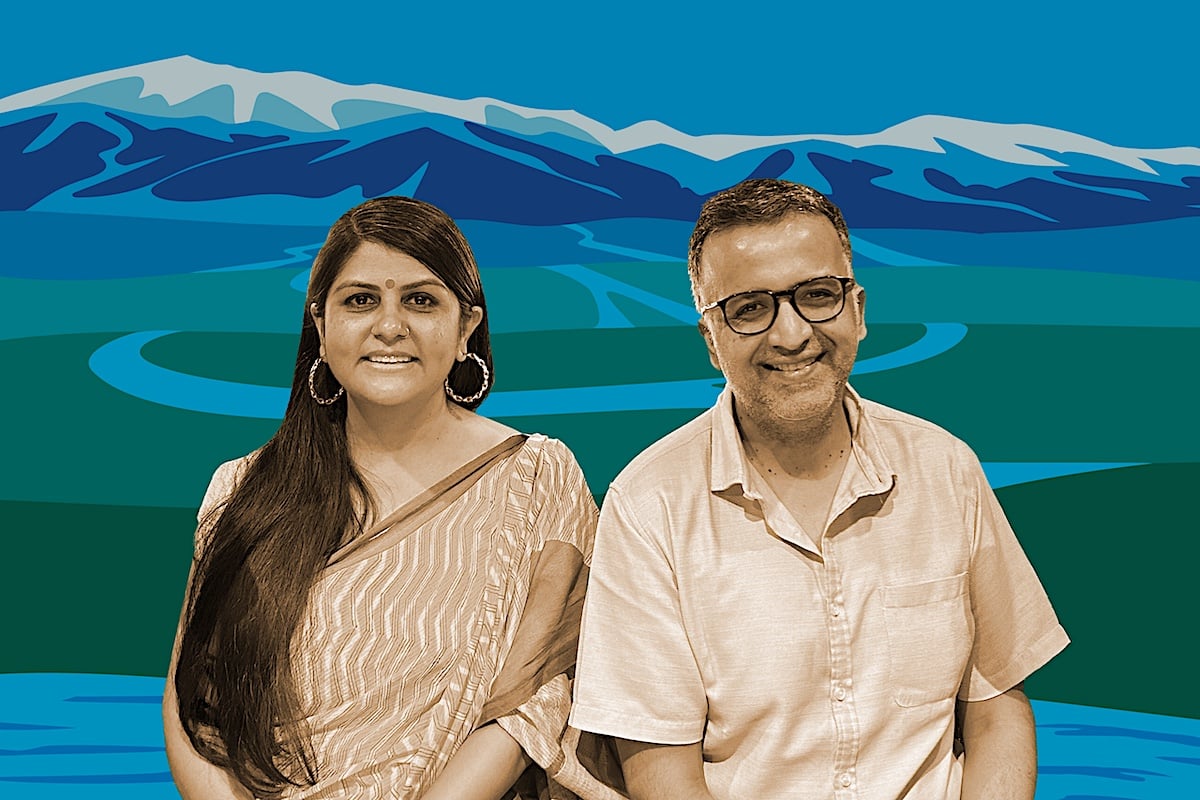 A man and woman sit next to each other, with the view of a mountain range in the background