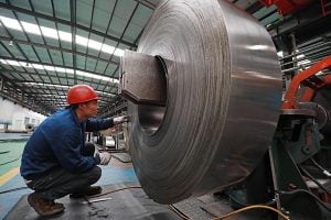 Worker examining a large coil of steel in an industrial setting.